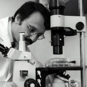 grayscale photography of doctor using microscope