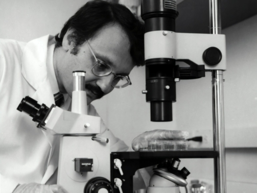 grayscale photography of doctor using microscope